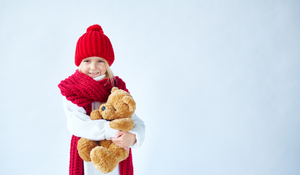 Girl in a red scarf and hat hugging a teddy bear.