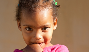 non-verbal child looking at camera with hand to mouth